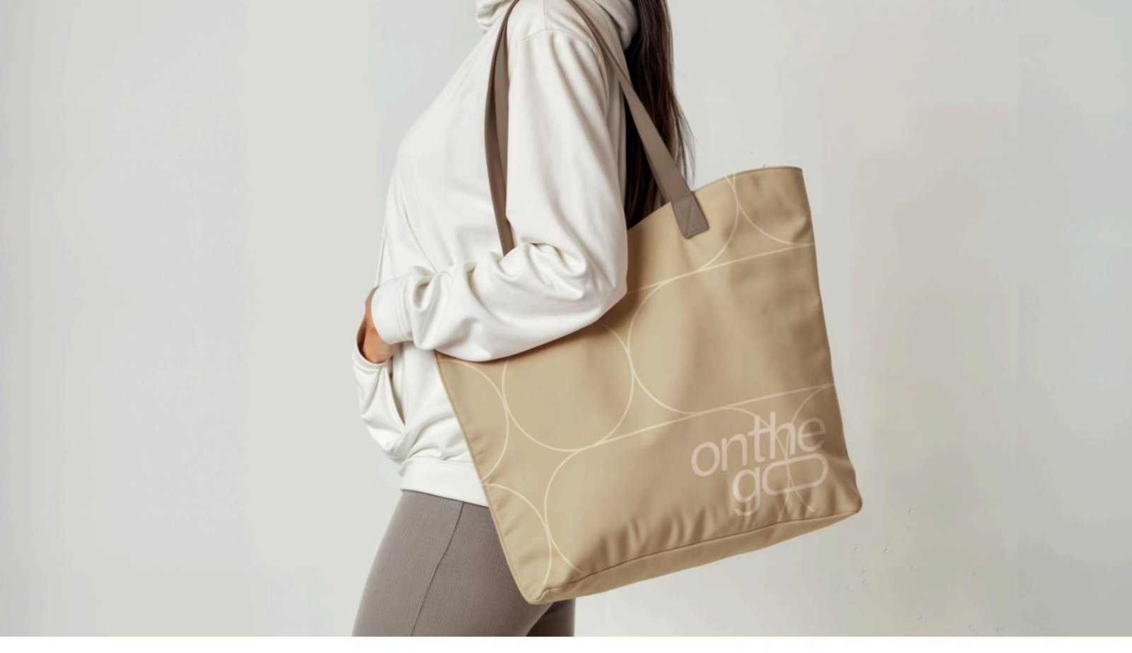 Woman in white hoodie carrying an OnTheGo branded tote bag